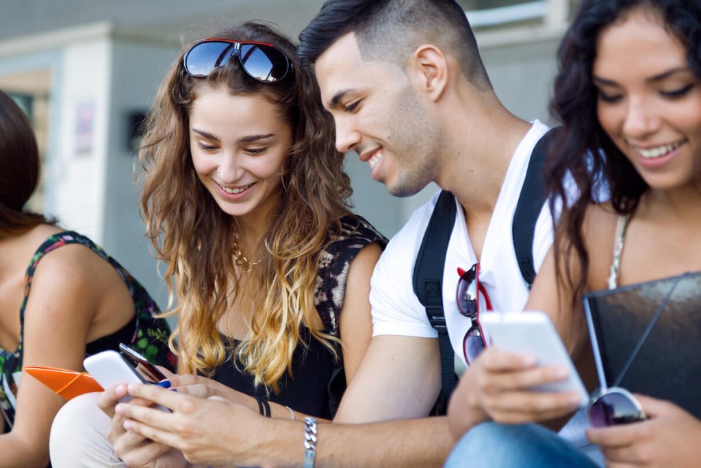 Young students smiling and interacting with their smartphones after class