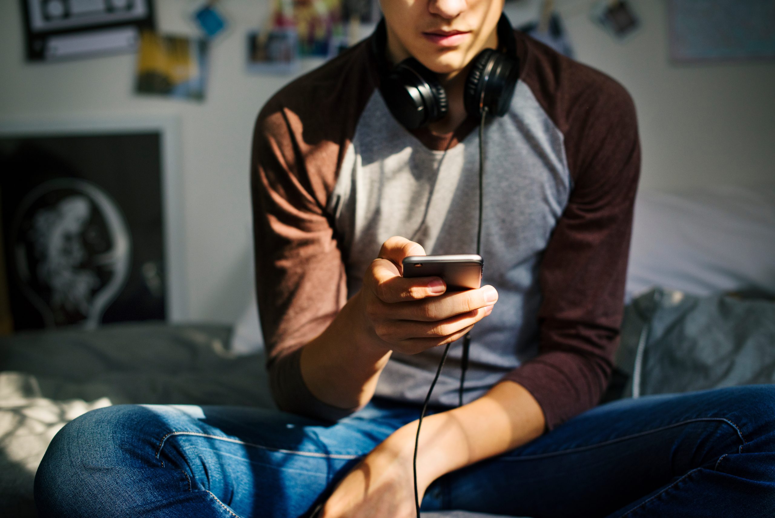 Teenage boy in a bedroom listening to music through his smartpho