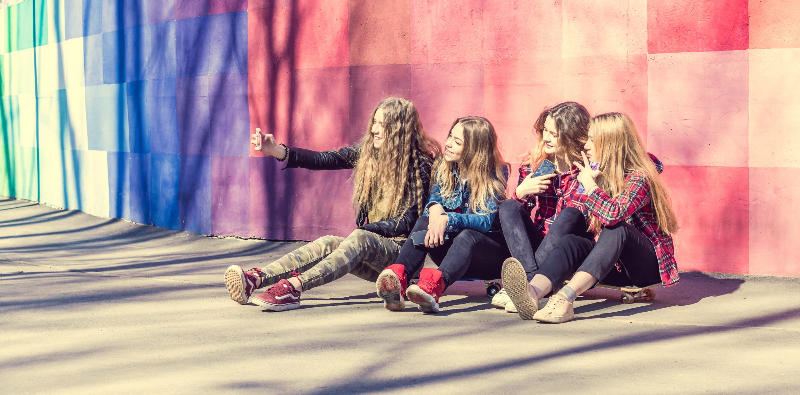 Teenage girls making selfie outdoors while sitting on longboards. Happy friends in the park on a sunny day.